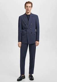 Costume bleu marine à double boutonnage avec une coupe ajustée, une texture lisse et des accents noirs. Associé à des chaussures noires pour un look formel.
