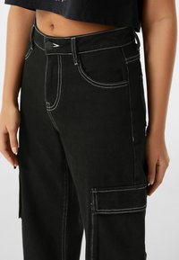 Svarta cargobyxor i denim med vit söm. Har fram- och sidofickor, en figursydd midja och en avslappnad passform på benen.