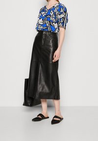 Falda midi de cuero negra combinada con una blusa de estampado floral en azul y blanco. Unos zapatos negros sin cordones completan el conjunto.