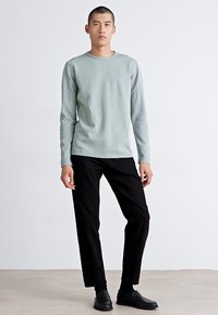 Lichtgroene geribbelde longsleeve met zwarte broek. Het shirt heeft een ronde hals en een gestructureerde stof. Eenvoudige ontwerpelementen.