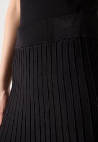 Zwarte geribbelde gebreide rok met een brede elastische tailleband; heeft verticale strepen en een gestructureerde afwerking. Ontworpen voor een slim fit.