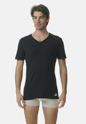 Czarny t-shirt z dekoltem w serek wykonany z bawełny, z krótkimi rękawami i subtelnym białym logo marki na dole po lewej stronie z przodu. Model nosi szare szorty.
