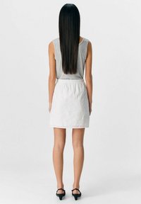 Top gris sin mangas y falda blanca con bordados florales. La falda tiene una cinturilla elástica y dobladillo. Se lleva con zapatos de tacón altos negros.