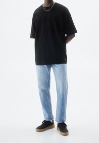 T-shirt nera in cotone con vestibilità ampia, abbinata a jeans in denim azzurro chiaro e sneakers nere con suola in gomma color naturale. Accessorio a catena argentata.