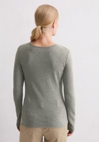 Langärmliges grünes Shirt aus weichem Stoff mit rundem Halsausschnitt, taillierter Passform und glatter Textur, getragen mit beigen Hosen.