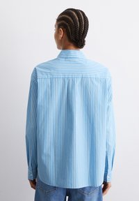 Camicia a maniche lunghe a righe blu realizzata in tessuto leggero, con polsini bottonati e piega sul retro per facilitare i movimenti. Accompagnata da jeans in denim casual.