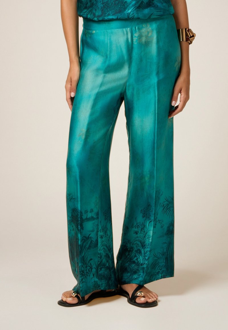 Türkise weit geschnittene Hose aus einem seidig-glänzenden Gewebe mit einem botanischen Druck entlang des Saums. Glatte Textur und ein geraffter Bund für zusätzlichen Komfort.