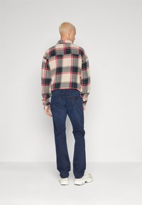 Cămașă flanelată în carouri, bej, roșu și bleumarin, cu guler și mâneci lungi, asortată cu blugi de culoare albastru închis și adidași de nuanță deschisă.