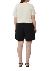 T-shirt crème raccourci à manches courtes associé à un short noir, avec une taille élastique et une texture de tissu lisse. Des sandales noires complètent le look.