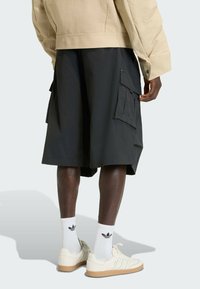 Black cargo shorts with side pockets, paired with white socks featuring a black logo and cream-colored sneakers with a gum sole.