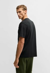 Sort t-shirt med rund hals og korte ærmer, lavet af blødt bomuldsstof. Pasformen er afslappet, og den er sat sammen med mørkegrønne bukser.