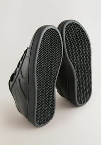 Baskets noires avec un dessus en cuir lisse, semelles en caoutchouc texturé présentant un motif en chevrons, et système de laçage à l'avant.