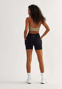 Black athletic shorts with pockets paired with a light brown sports bra featuring a crisscross back design. White socks and sneakers complete the look.