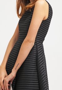 Robe noire sans manches avec une texture à rayures horizontales, corsage ajusté et jupe légèrement évasée, mettant en valeur des détails en tissu complexes.