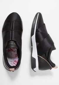 Chaussures de sport noires avec une tige en tissu texturé, des bandes élastiques croisées et une semelle en caoutchouc blanche. Doublure intérieure à motif floral et accents en or rose.