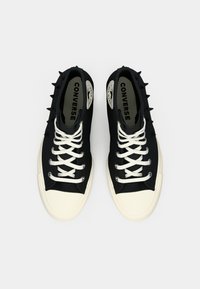 Pár čiernych vysokých teniskových topánok Converse s bielymi šnúrkami, krémovými špičkami a čiernymi hrotmi na stranách, z pohľadu zhora.