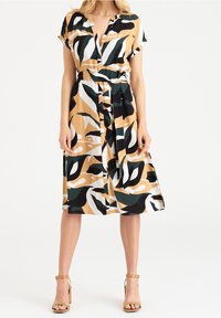 Kortärmad klänning i beige med ett djärvt mönster av svarta, vita och gröna blad, midjebälte och knälång A-linjeform.