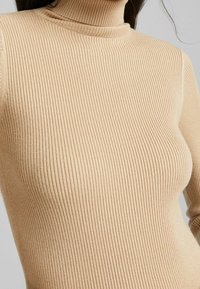 Maglione beige a collo alto con costine realizzato in un tessuto a maglia testurizzato. Presenta una silhouette aderente e un collo alto.