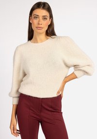 Lichtbeige, fluffy trui met een ronde hals en ballonmouwen, gecombineerd met bordeauxrode broeken. Zachte textuur, casual ontwerp en relaxte pasvorm.