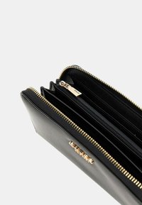 Billetera de cuero negro con cremallera y herrajes en dorado. El interior cuenta con múltiples ranuras para tarjetas y un compartimento con cremallera para monedas.