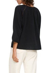 Czarna, luźna bluzka wykonana z teksturowanej tkaniny. Posiada zaokrąglony dekolt oraz rękawy o długości trzech czwarte z subtelnymi detalami wzdłuż szwu.