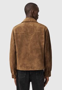 Ruskea mokkatakki, jossa on terävä kaulus, takana pala, jossa yläosa erottuu, ja joustavat hihansuut. Pehmeä tekstuuri, lyhyt pituus ja yksinkertainen muotoilu.