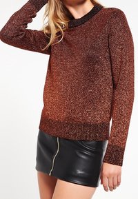 Suéter brillante de color cobre con un cuello y puños negros acanalados, combinado con una mini falda de cuero negra con un cierre frontal.