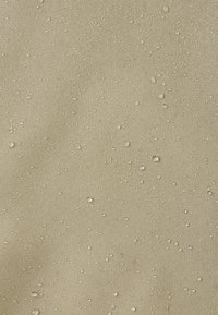 Surface en tissu beige avec des gouttelettes d'eau dispersées en perles sur le dessus, indiquant une texture de matériau résistant à l'eau.