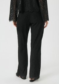 Sorte blondebukser med bred benstil, der har et blomsterprint og frynset kant. Stoffet har en tekstureret finish.