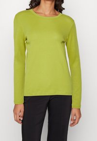 T-shirt a maniche lunghe in cotone verde brillante con scollo rotondo, caratterizzato da una texture morbida e dettagli di cucitura minimi, abbinato a pantaloni scuri.