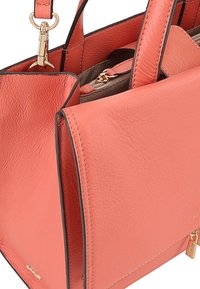 Koraal leren handtas met een gestructureerd ontwerp, voorzien van gouden hardware, contrasterende zwarte randen en dubbele handvatten voor het dragen.