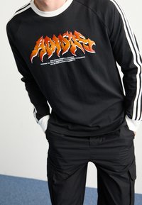 Svart crew-neck sweatshirt med vita ränder på ärmarna, med djärv text i orange och gult i flamastil på framsidan.