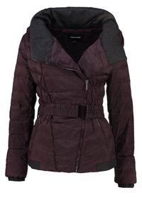 Veste matelassée violet foncé avec large col gris, fermeture éclair frontale asymétrique, taille ceinturée et poches latérales zippées.
