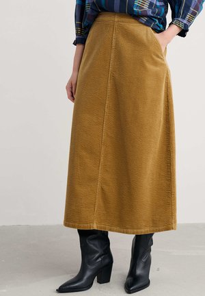 Bruine corduroy midi-rok met een rechte snit en gestikte plooien. Voorzien van een tailleband en zijzakken, gecombineerd met zwarte haklaarzen.