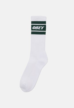 Un calzino in cotone bianco presenta un design a costine con una banda verde contenente la parola "OBEY" in lettere bianche.