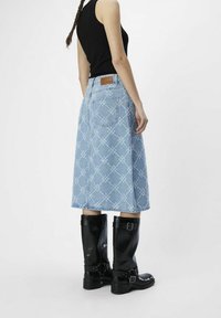 Vaaleansininen farkkuhame, jossa on teksturoitu kukkakuosi, varustettuna takataskuilla ja yhdistettynä mustiin polvipitkiin nahkabootseihin.