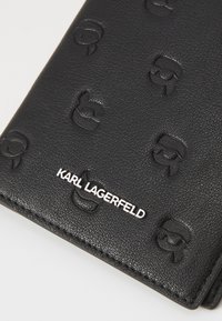 Juodas odinis piniginis, turintis reljefinius logotipus, tekstūruotą paviršių ir sidabrinę "KARL LAGERFELD" ženklinimą apačioje.