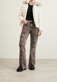 Höyhenpaita kermanvärisenä turkiskaulus hupulla, yhdistetty kuluneihin ruskeisiin cargo-farkkuihin, joissa on painonapitaskut ja halkiot lahkeissa, yhdistettynä mustiin korokepohjakenkiin.