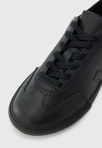 Μαύρο δερμάτινο αθλητικό παπούτσι με υφή, διαθέτει πλεγμένα  κορδόνια, στρογγυλεμένη μύτη και λαβιδωτή ελαστική σόλα με σχέδιο. Απλά διακοσμητικά στοιχεία.