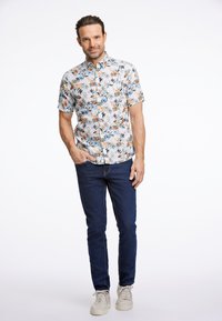 Camicia a maniche corte con un motivo floreale in vari colori, abbinata a jeans blu scuro e sneakers chiare.
