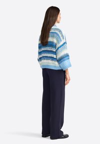 Maglione a maglia con righe blu e bianche, caratterizzato da una vestibilità ampia e maniche larghe, abbinato a pantaloni scuri a gamba larga. Texture morbida.