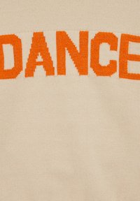 Beige tröja med stora, texturerade orangea bokstäver "DANCE" över bröstet. Materialet verkar mjukt med ett subtilt stickat mönster.