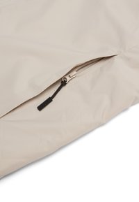 Primer plano de una tela beige con una cremallera parcialmente abierta y una lengüeta negra sobre una superficie lisa.