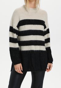 Musta ja kerma-valkoinen raidoitettu neulepaita, jossa on korkea kaulus, pitkät hihat ja rento istuvuus. Valmistettu pehmeästä, teksturoidusta neuleesta.