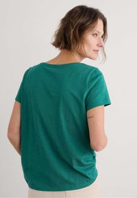 T-shirt verde a maniche corte con una vestibilità rilassata, scollatura rotonda e una texture morbida. Presenta un delicato motivo melange. Senza hardware prominente.