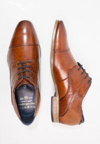 Chaussures habillées en cuir marron avec une finition lisse, des détails perforés sur le côté et une semelle marron fine. Les lacets sont foncés pour créer un contraste.