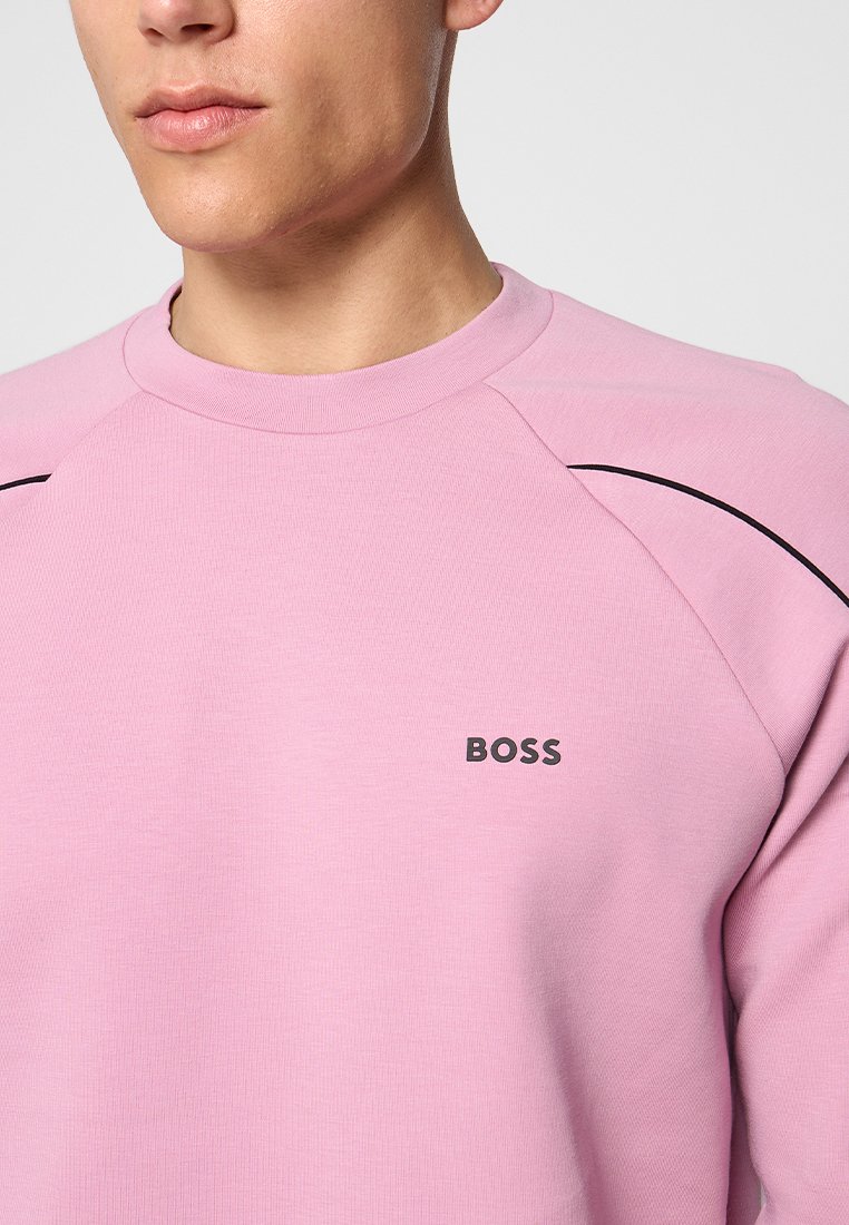 Homme portant un sweat-shirt rose clair avec des bordures noires aux épaules et le logo "BOSS" sur la poitrine gauche.