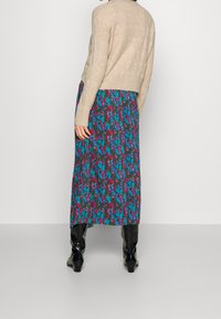 Knit beige sweater paired with a long, patterned skirt featuring green, purple, and pink designs, worn with black knee-high boots.