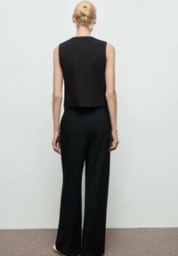 Zwarte cropped mouwloze top, gecombineerd met wijde zwarte broek, met een soepele textuur en minimalistisch ontwerp, gezien van achteren.