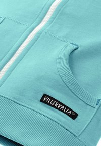 Jasnoniebieska bluza z kapturem na zamek, wykonana z miękkiej bawełny, z prążkowanymi mankietami i dołem. Posiada przednią kieszeń oraz czarną metkę z logo.